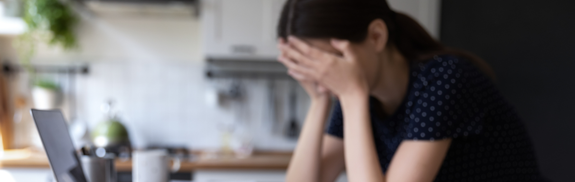 Stressed woman looking at her computer and her bills at the kitchen table